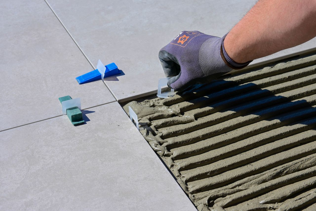 services-04 Detailed view of gloved hand aligning tiles with levelers and spacers during construction.