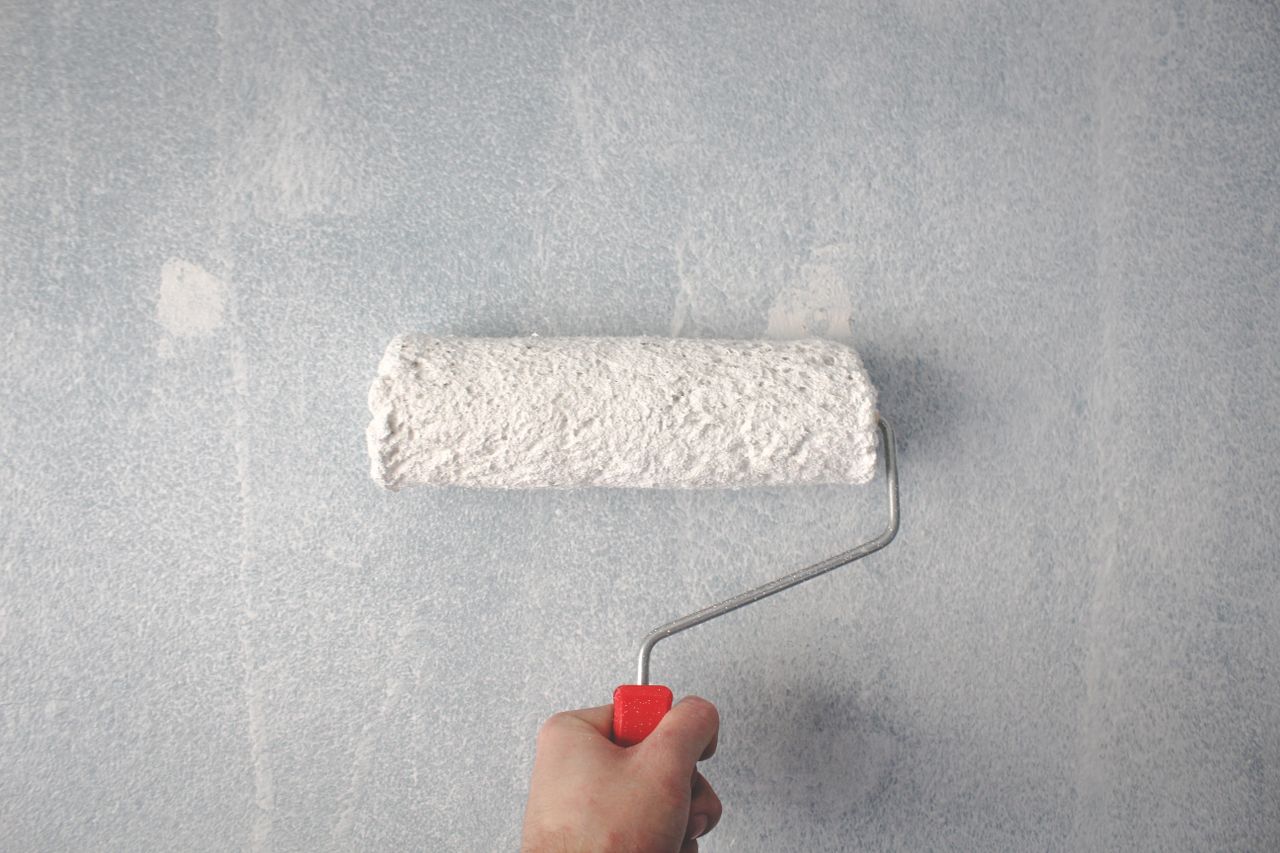 services-03 A person's hand using a paint roller to apply white paint on a wall.